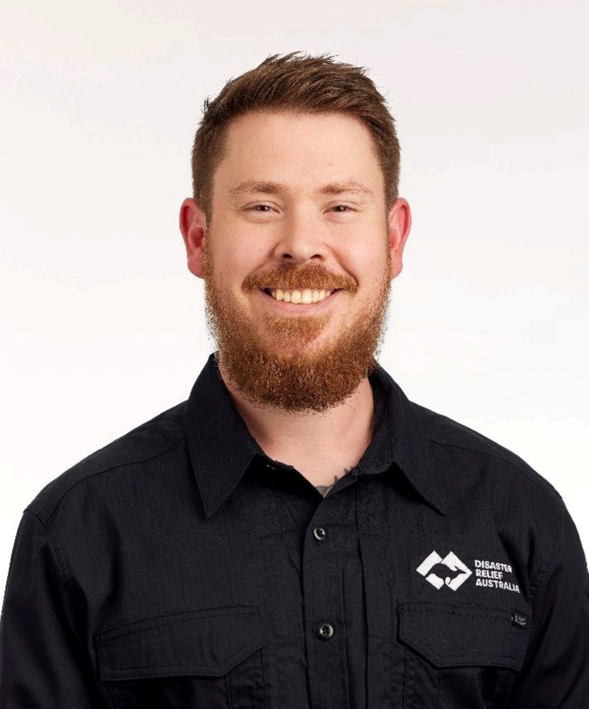 Headshot of a smiling dark-haired man in a black polo with a DRA logo