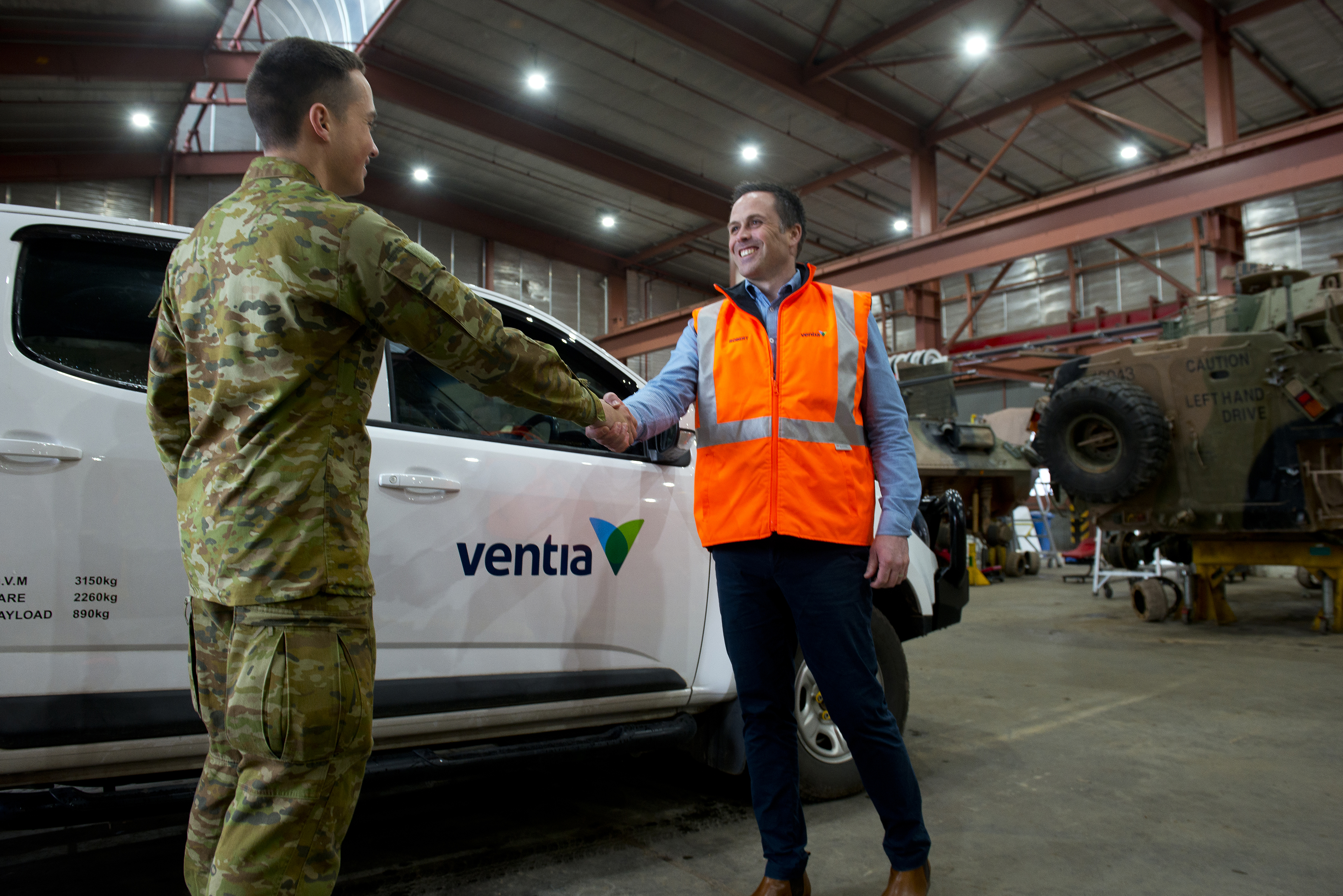 A man in camo gear shakes hands with a man in a high vis vest in front of a Ventia branded ute