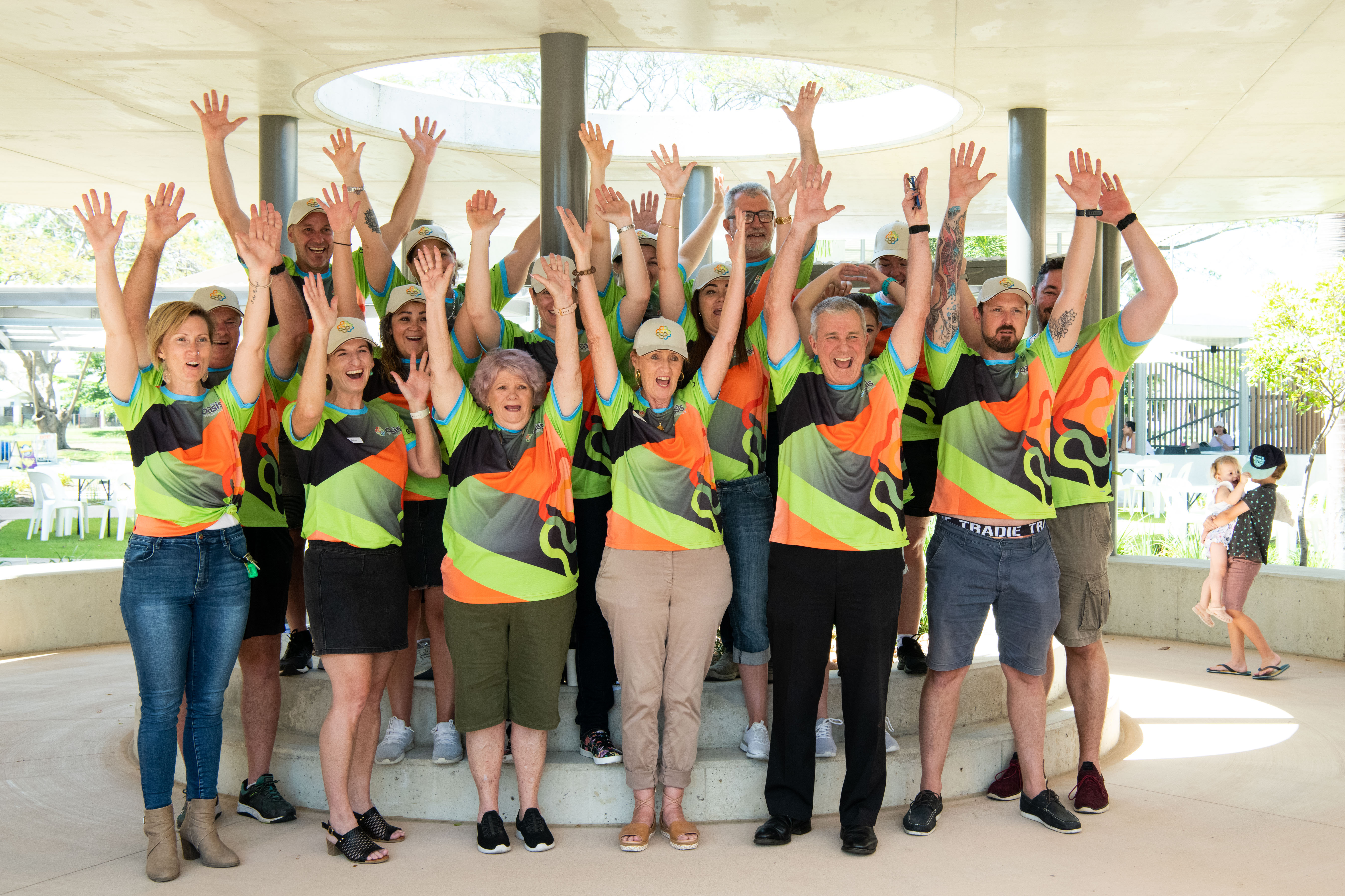 A group of people standing with their hands up in the air, smiling, wearing matching t-shirts