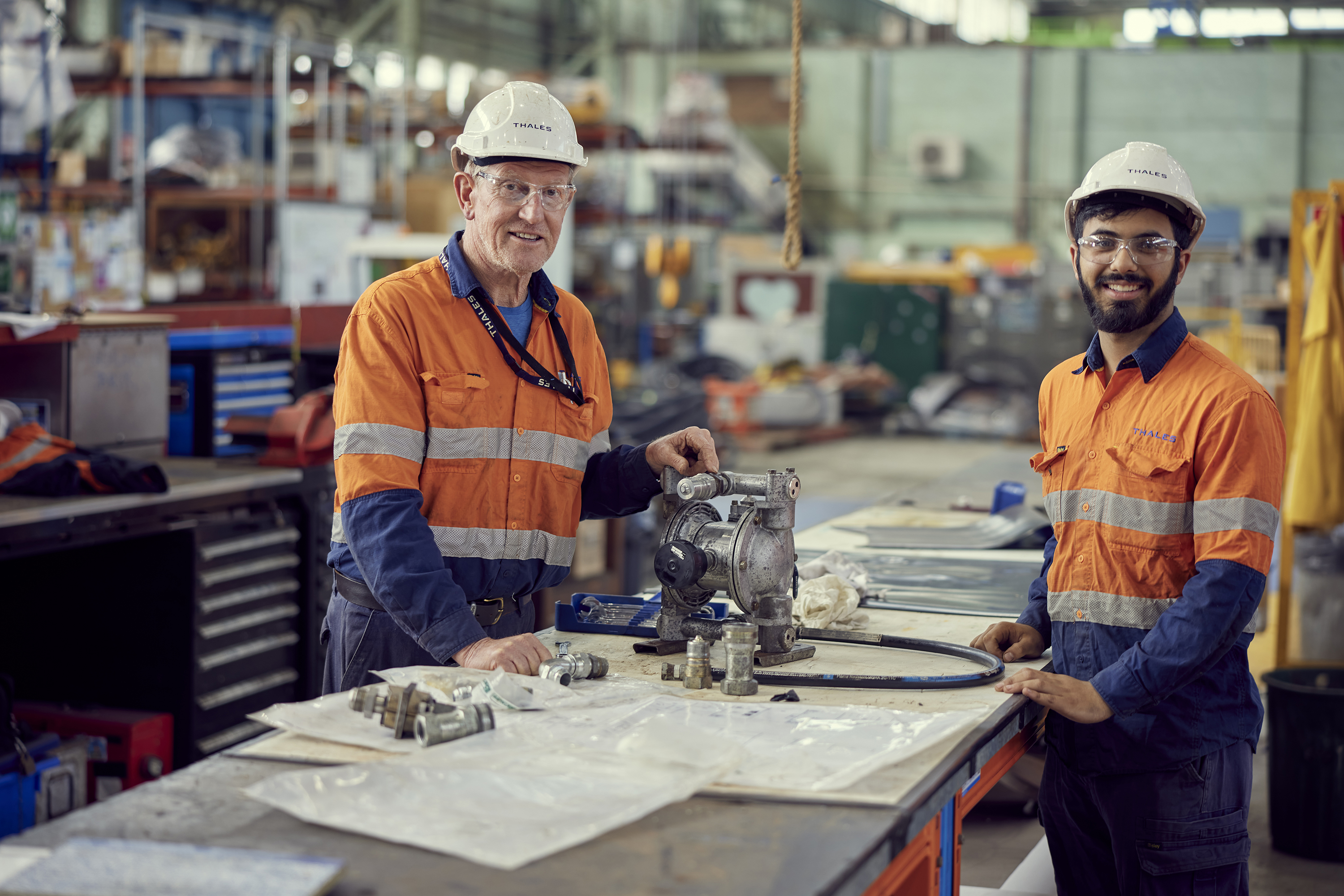 Two men in high vis and safety helmets in a workshop