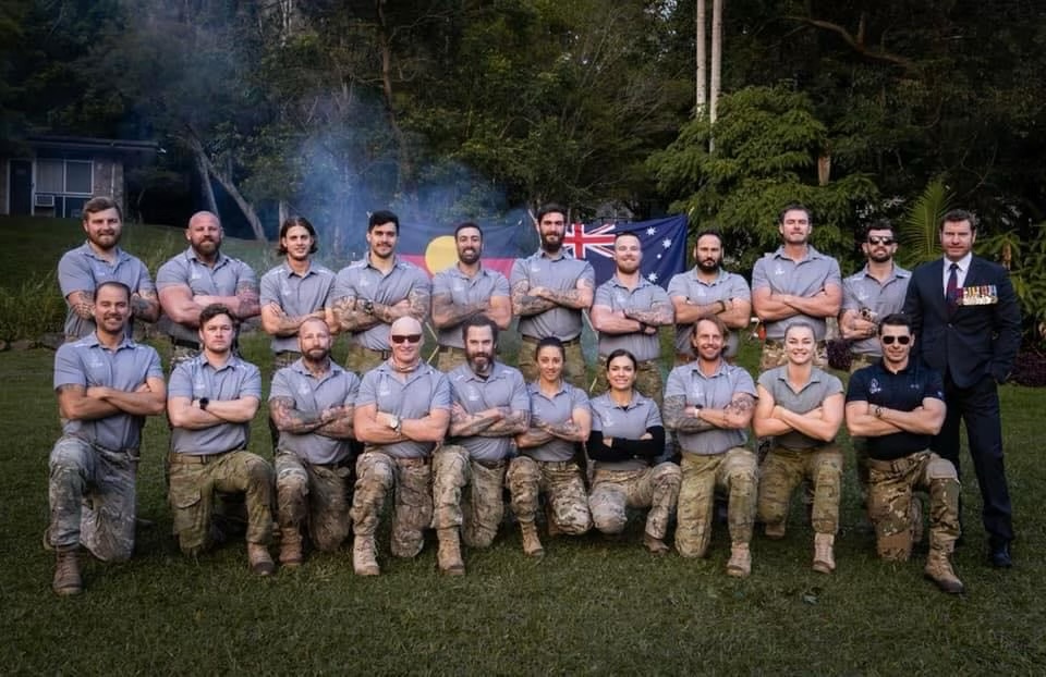 Two rows of people in matching polos and camo trousers in front of the Australian and Aboriginal flags