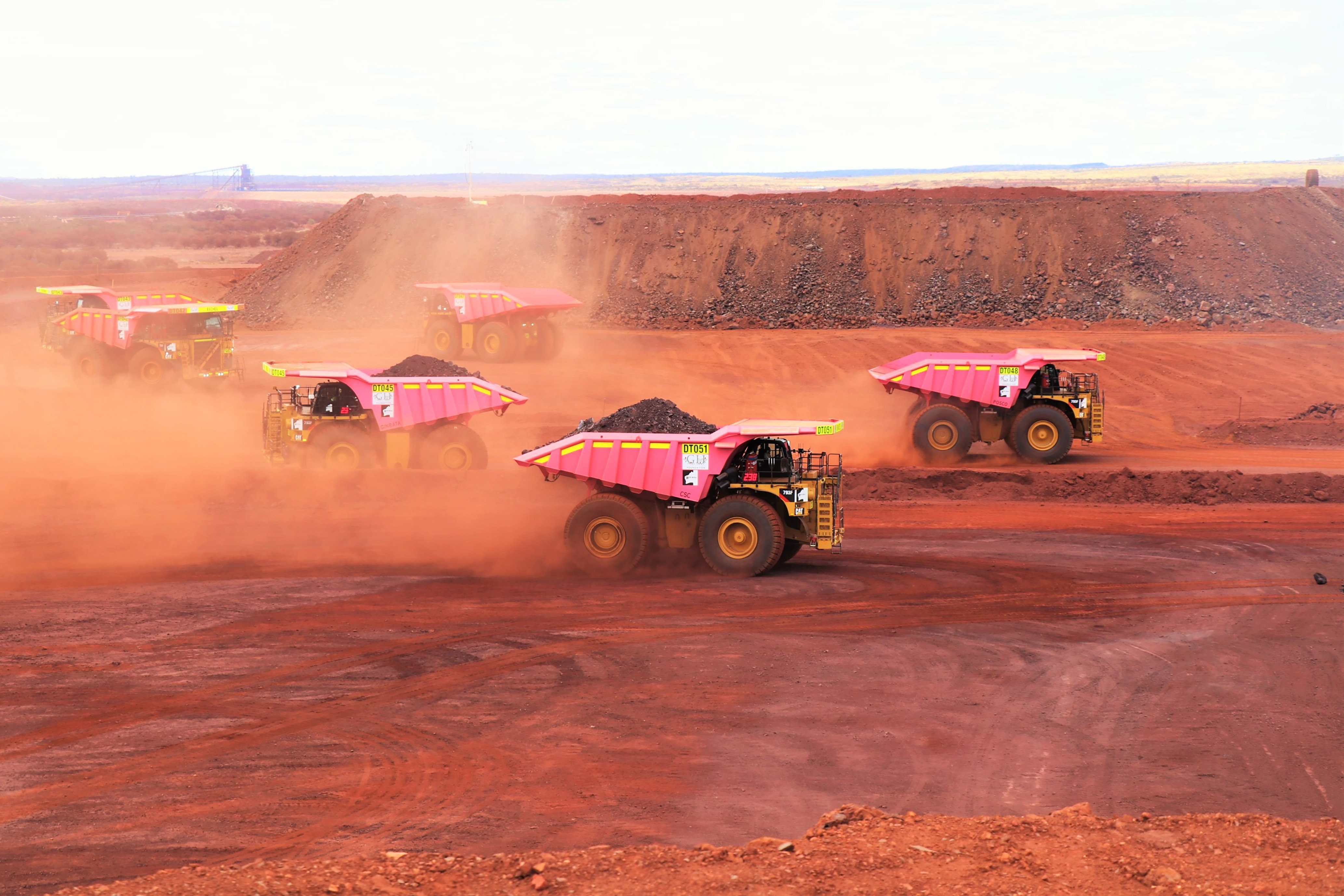 Several pink mine trucks in a red dirt pit