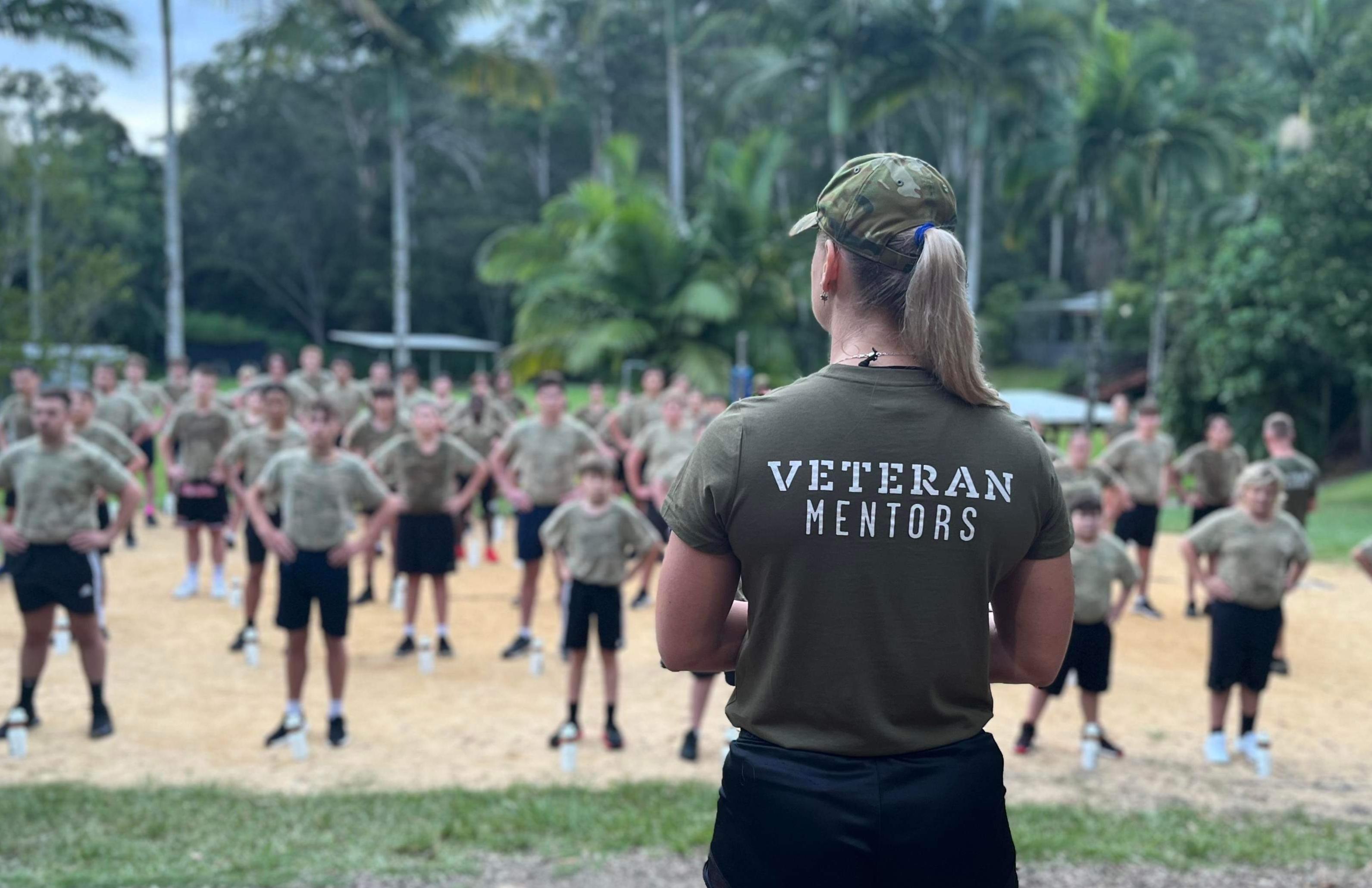 Blonde woman in a Veteran Mentors tshirt surveys youths standing in lines