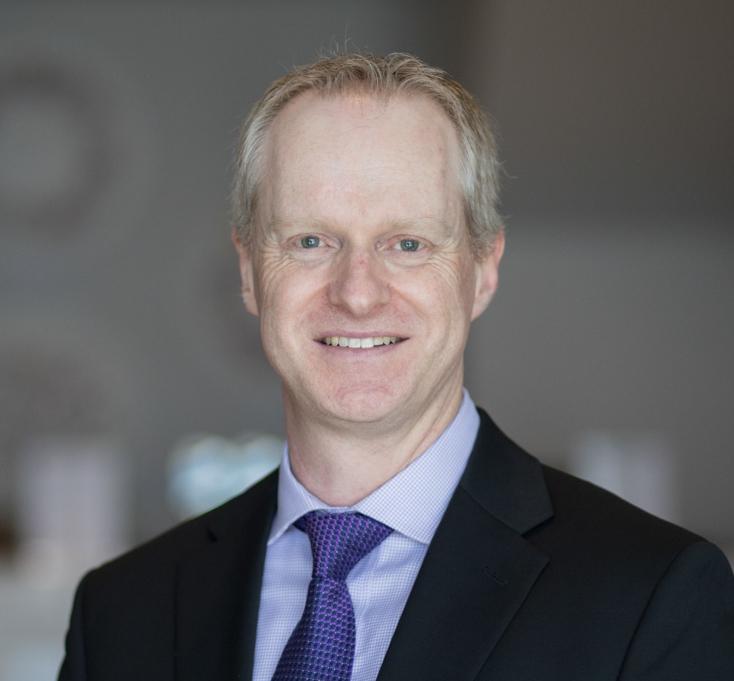 A headshot of a smiling white man in a suit and tie