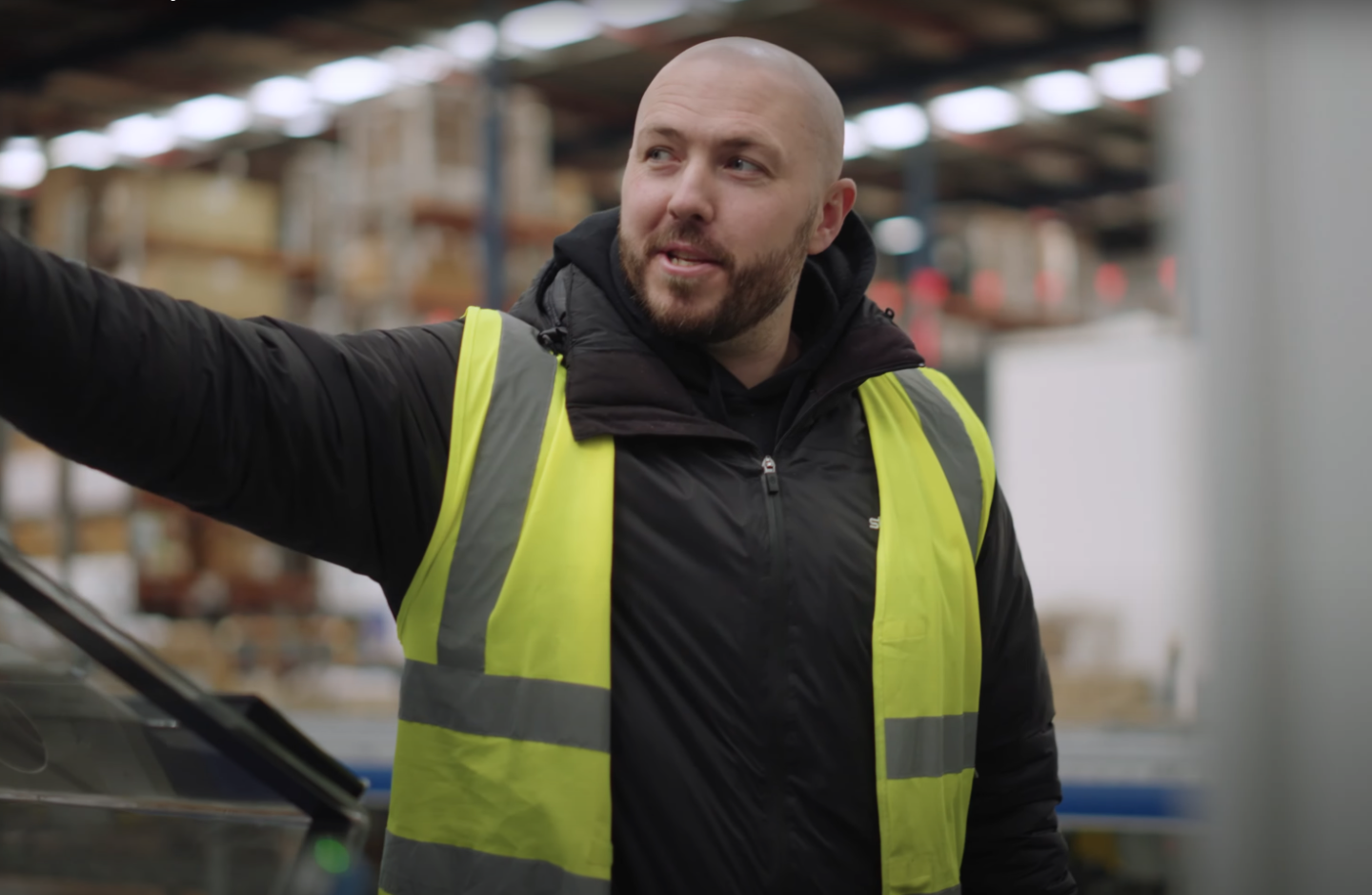 A man in a black jacket and yellow high-vis gestures out of shot