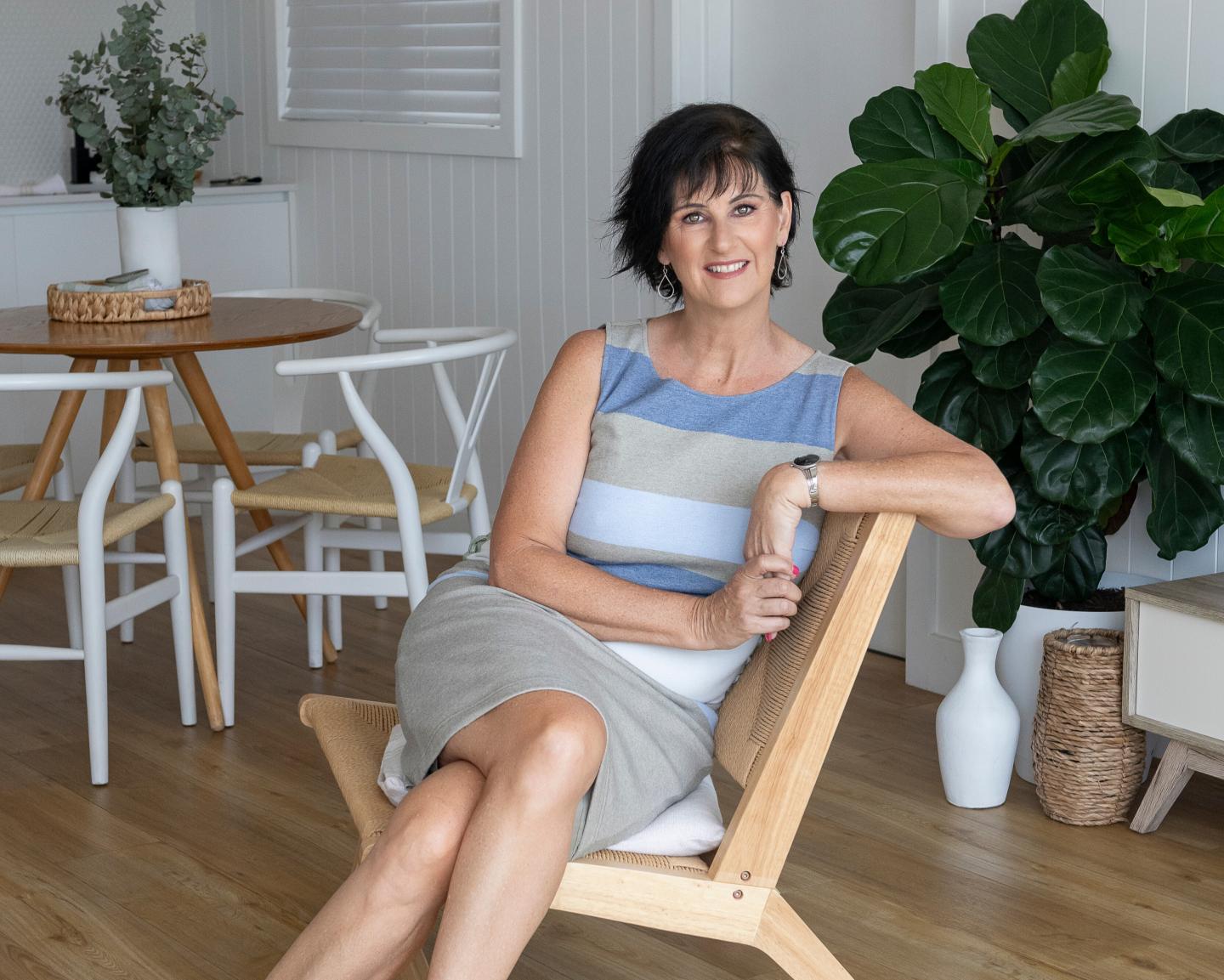 A woman with short dark hair leaning back in a wooden chair