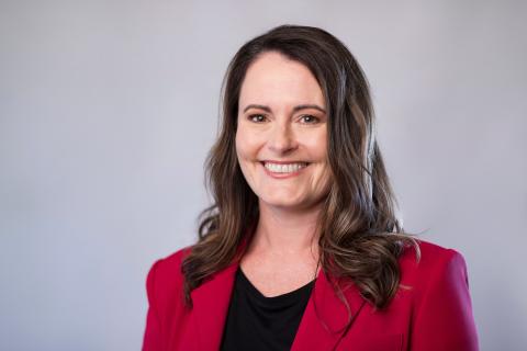 Headshot of a dark-haired, smiling woman in a black top and red blazer