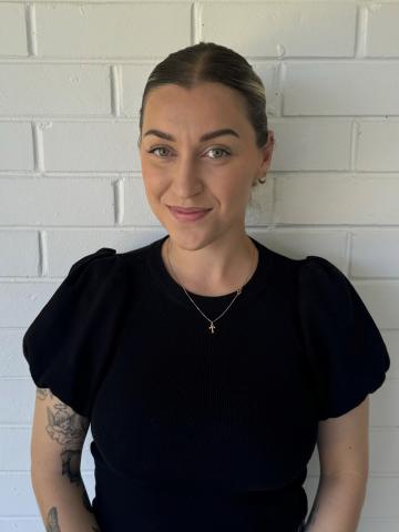 A woman in a black shirt poses in front of a white brick wall